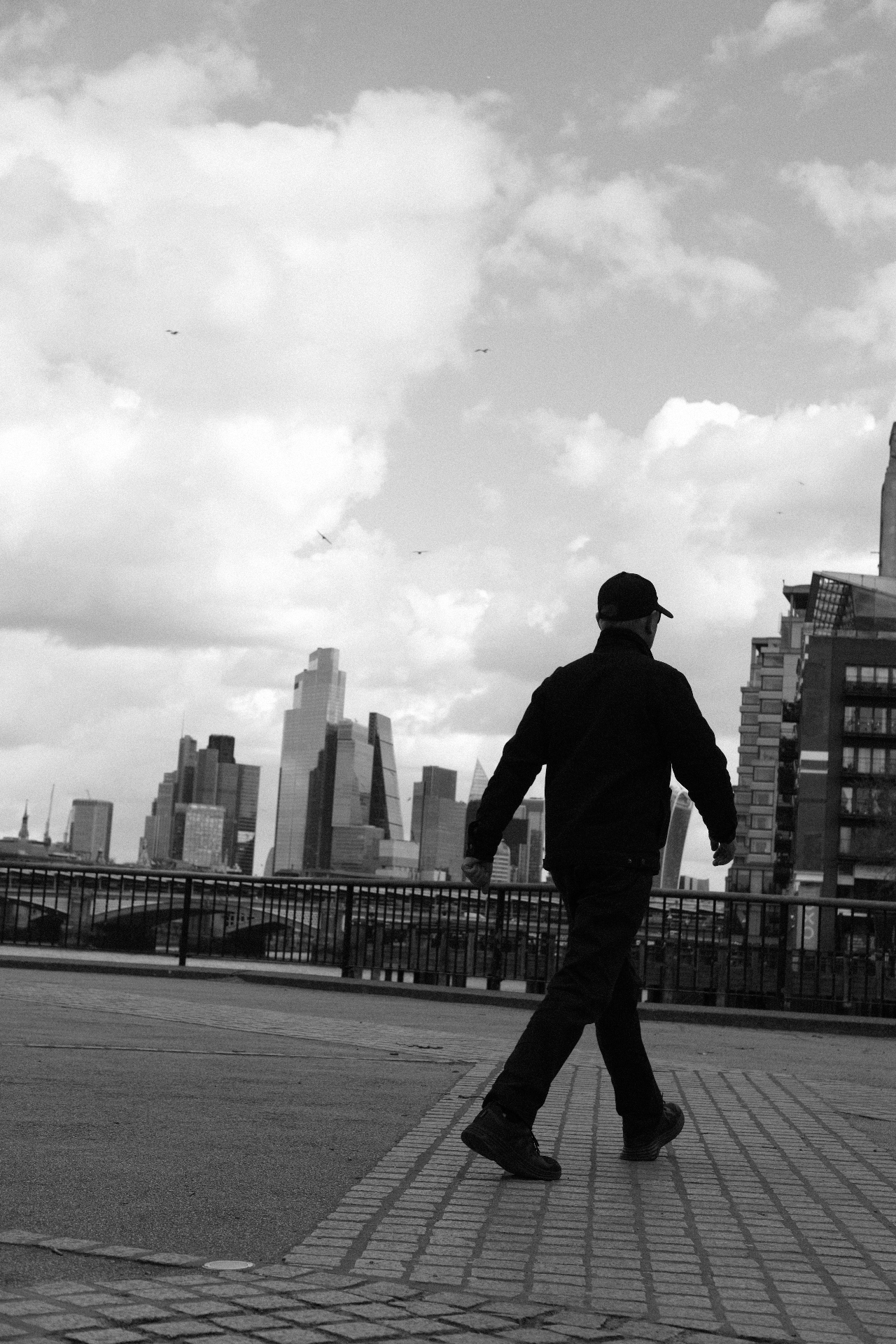 Strides, London City — a figure mid-stride on the riverside walkway with the City skyline behind.