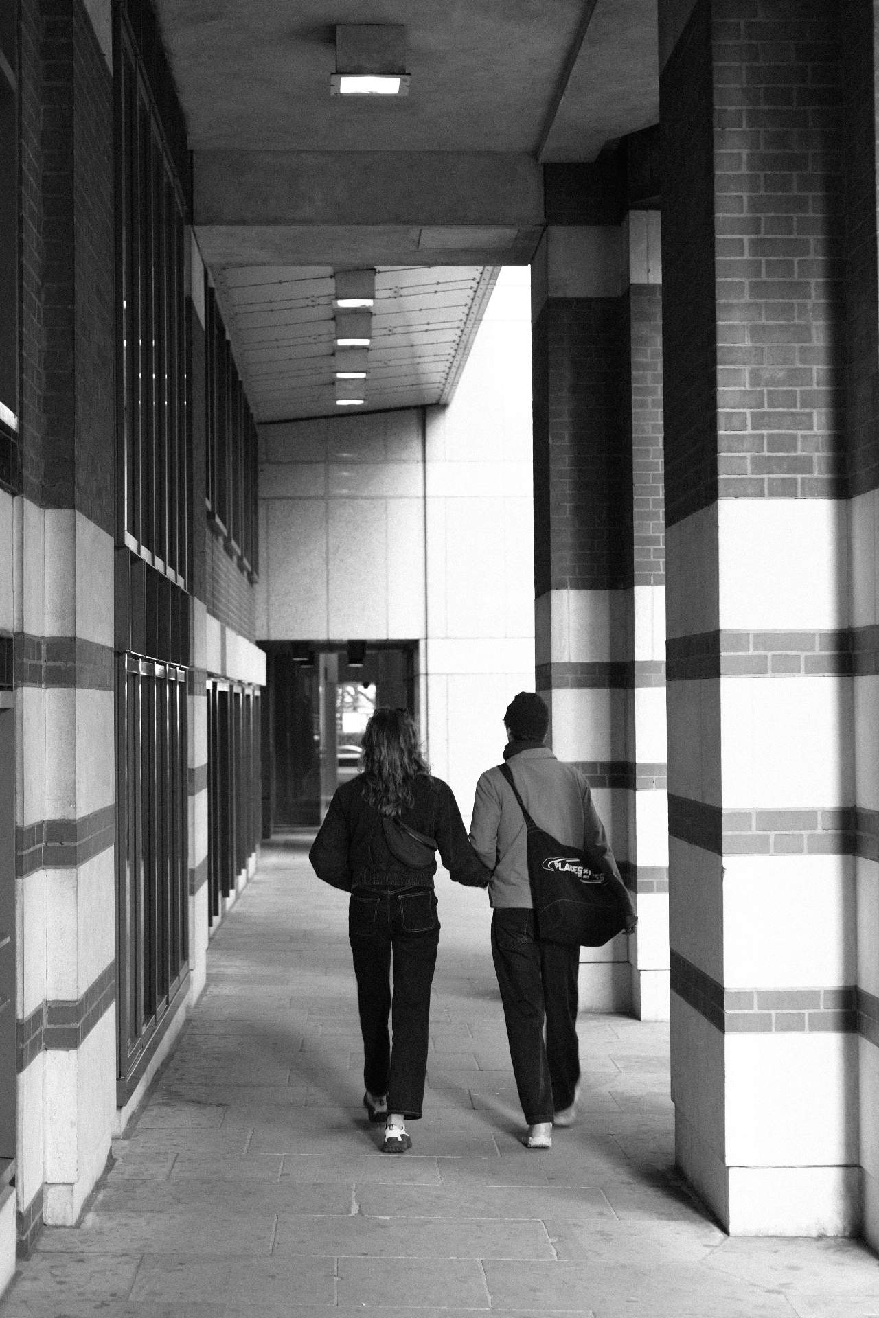 A couple walking hand in hand through a striped brick colonnade.